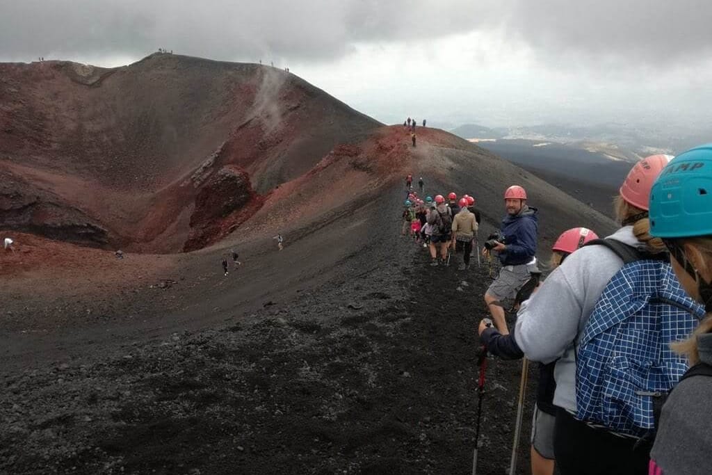 Escursionisti in fila sul crinale del cratere, tra sabbie rosse e vapore