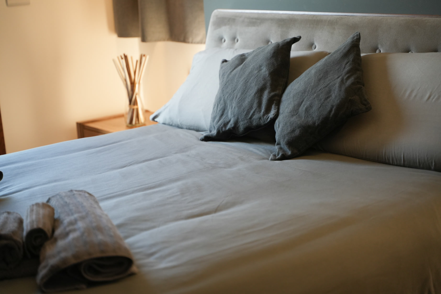 Letto rifatto con cuscini grigi nella suite Aera, luce laterale calda