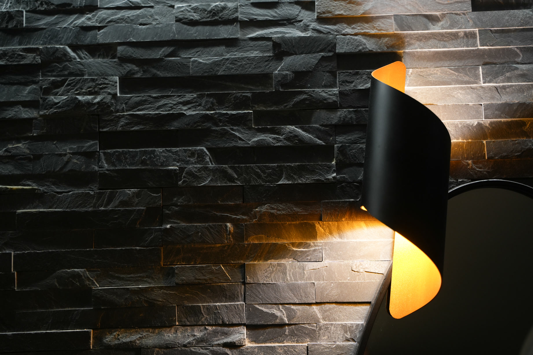 Parete in pietra lavica nera illuminata da un'applique nera e oro